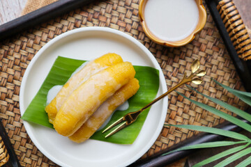 Baby bananas in syrup with coconut milk on top served on bamboo tray at top view - Thai dessert called Kluay Kai Cheum