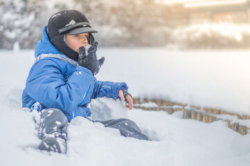 Fototapeta na wymiar A happy boy plays snowballs and eats snow on the snowy ground
