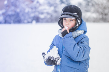 A happy boy plays snowballs and eats snow on the snowy ground