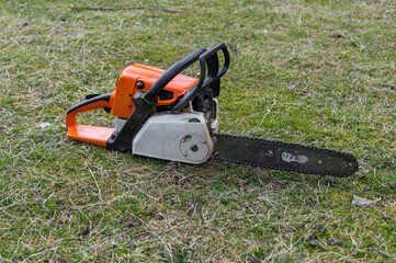 Naklejka premium Gasoline powered professional chainsaw. Chain saw for cutting wood on green grass. Cut tree machine