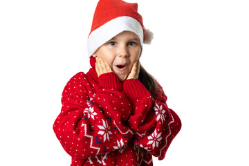 portrait of excited, charming girl in red Santa Claus hat in red Christmas sweater with reindeer touching face with palms, isolated on white background. 
