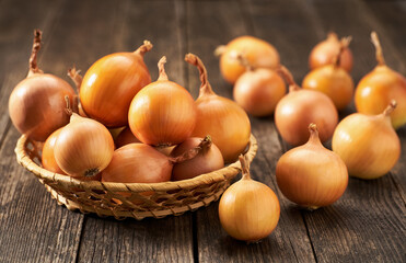 yellow onions in a basket on a wooden table.