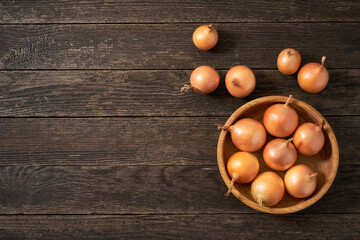 yellow onions in a wooden bowl on a rustic wooden table.