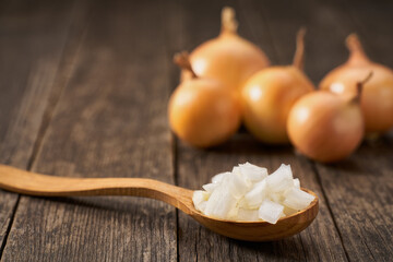 Chopped onion in a wooden spoon on a rustic table.