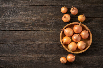 yellow onions in a wooden bowl on a rustic wooden table.