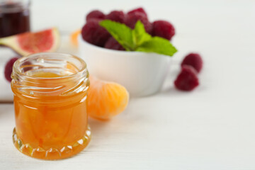 Open glass jar of sweet jam on white wooden table, closeup. Space for text