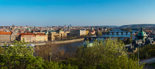 Obraz premium Wide panoramic aerial view of Prague Old Town architecture roof top and Charles Bridge over Vltava river seen from Letna hill park, spring sunny day, blue sky, Czech Republic