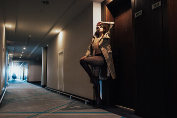 young beautiful girl in the hotel corridor, wearing a long trench coat and high boots