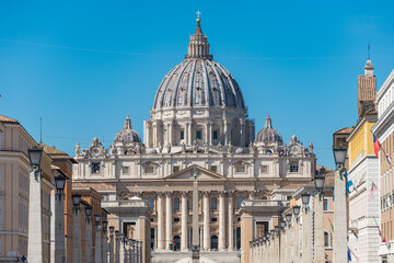 The dome of Saint Peter's Basilica and its statues of saints at St. Peter's Square, Vatican City view from Via della Conciliazione in Rome, Italy. Pine tree at the foreground.