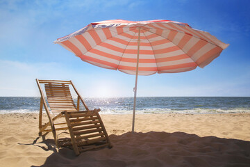 Deck chair near red and white striped beach umbrella on sandy seashore