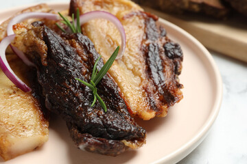 Tasty fried pork lard with rosemary and onion on white table, closeup