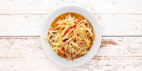 Som Tum Pla Ra, Thai E-San food, spicy papaya salad with pickled fish, tomato, lime and chilli in white ceramic plate on white wood texture background with copy space for text, top view