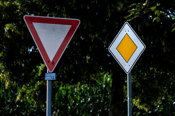 Zwei gegensätzliche Verkehrsschilder: Vorfahrt achten und Vorfahrtstraße