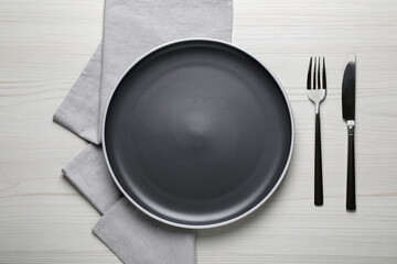 New dark plate and cutlery on white wooden table, flat lay