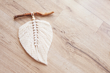 Macrame leaf  in natural color and thread windings lying on a wooden table. Cotton rope decor macrame to make your room more cozy and unique. Woman hobby. Handmade wall hanging decor. Copy space