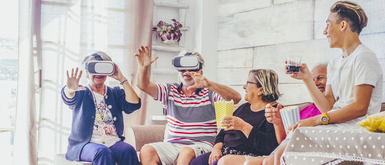 Group of mixed ages people have fun all together during celebration - senior grandfathers and grandson boy laugh a lot using goggles vr technology to play and have fun indoor at home