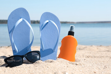 Stylish flip flops, sunglasses and sun protection spray on sandy beach - obrazy, fototapety, plakaty