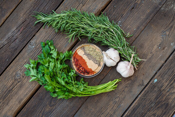 Naklejka na ściany i meble Fresh rosemary, parsley, spices and garlic on the wooden table background.