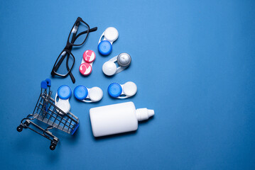 Contact lenses, eye glasses and eye solution bottle in the shopping cart on the blue flat lay background.