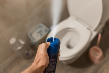 The guy's hand holds and sprays the air freshener in the toilet or bathroom. Home Hygiene Concept