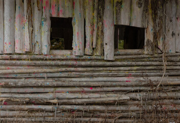vertical and horizontal logs of log cabin in woods in paint ball area two irregular shaped windows logs still peeling bark new shapes open windows paint splotches from paint ball paint horizontal 