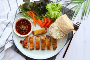 Grilled chicken serving with sticky rice and spicy dipping sauce and garnish with fresh vegetables...