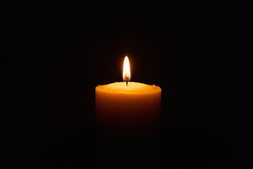 One single light candle burning brightly in the black background.Spiritual candle yellow flame....
