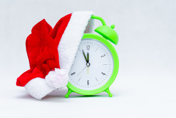 Alarm clock with Santa hat isolated on gray white background.Green clock with christmas red santa...
