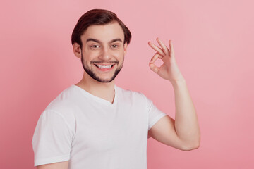 Portrait of dreamer guy raise hand show okay gesture beaming smile look camera on pink background