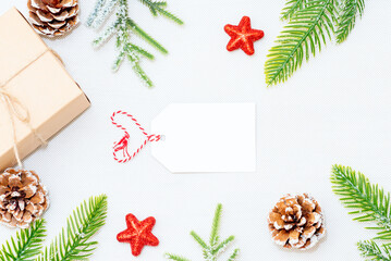 Christmas heart shape blank greeting card in frame of fir branches, decorations, gift box and cones over white background.mockup. flat lay. top view.