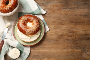 Delicious bagel with cream cheese on wooden table, flat lay. Space for text