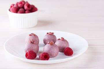 Pink truffles with raspberries on a white plate. Sugar, gluten and lactose free, vegan.