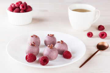 Raspberry truffles with a cup of tea on a light table. Sugar, gluten and lactose free, vegan.