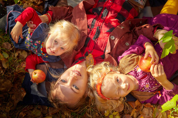 Two young little girl and his mother with blonde hair in an autumn park on a yellow and orange leaf background. Family walking in forest