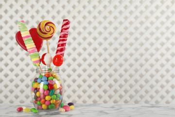 Jar with different delicious candies on white marble table, space for text