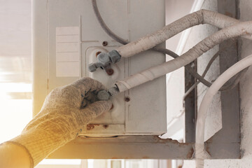 The hand of an air conditioner repair and maintenance specialist in a construction glove working...