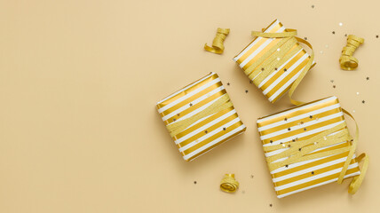 Gift boxes wrapped in golden paper with golden ribbon and confetti stars on beige background. New Year and Christmas greeting card with copy space