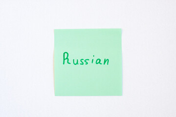 Top view flat lay of the reminder notepaper of green color with word Russian on it on white background. Flashcards and language studies concept