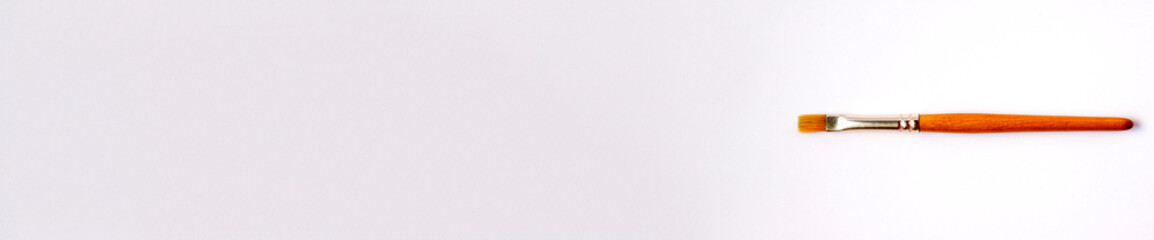 Flat lay banner of artistic orange metal wooden paint brush close up on white background with copy space from above. Drawing and design concept work tools on the right
