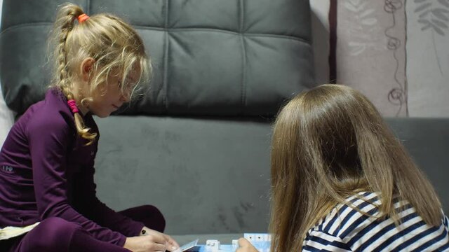 A Caucasian blonde girl plays a board game with a woman on the couch. The concept of a happy family
