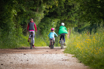 Mother, a son, and a preschool daughter cycling on a gravel road near the forest