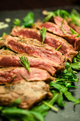Close up of Sliced beef meat, medium rare grilled, with rosemary and rocket salad on a plate