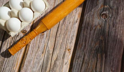 Fototapeta na wymiar white chicken eggs wooden rolling pin on wooden surface sun rays breakfast baking ingredients