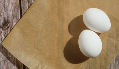 two white chicken eggs on parchment paper on a wooden surface sun rays