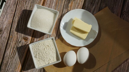 white chicken eggs bowls with sugar and flour butter on a saucer on a wooden surface sun rays breakfast baking ingredients
