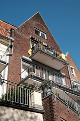 Wohnhaus mit Spitzgiebel, rotbrauner Klinkerfassade und großen Balkons vor blauem Himmel im...