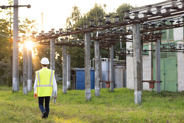 Electrical engineer wearing a helmet and safety vest walking near high voltage electrical lines...