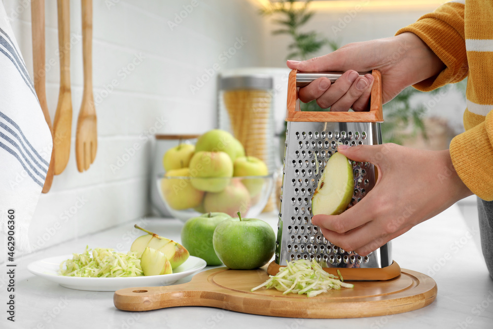 Wall mural woman grating fresh green apple at kitchen counter, closeup