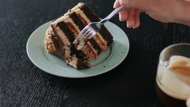 Woman cutting brownie cake with fork with coffee cup on wooden table in cafe
