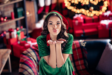 Photo of cheerful happy charming woman santa helper hold hands send air kiss you indoors inside...
